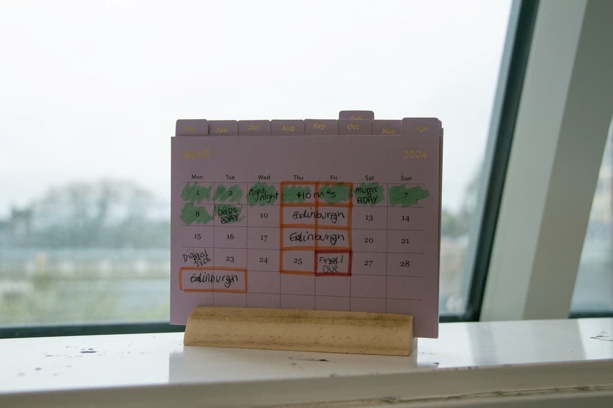 A physical paper desk calendar with handwritten notes propped on a windowsill.